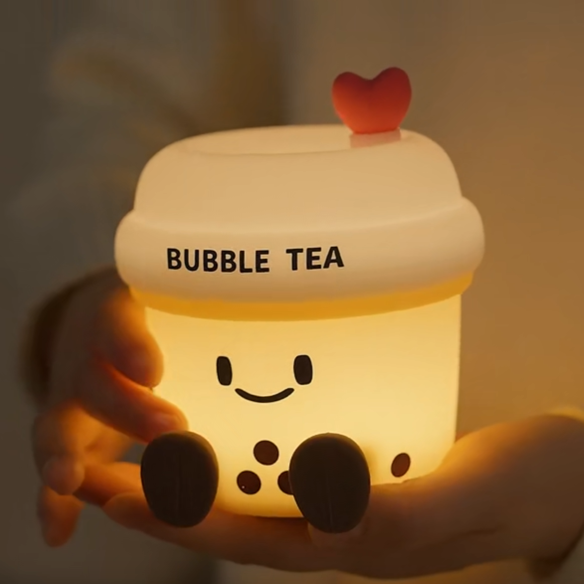 Luminous bubble tea-shaped container with a heart on top, held in hands against a warm background.