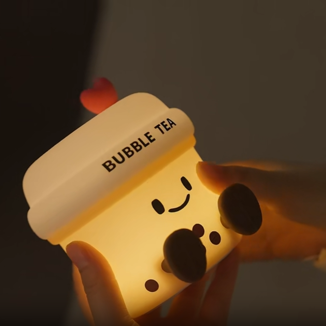 Cute, cartoon-style bubble tea cup with a smiling face held by a hand against a dark background