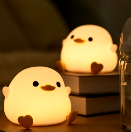 Two LED Night Light Lamp ducks sitting on top of a table with books