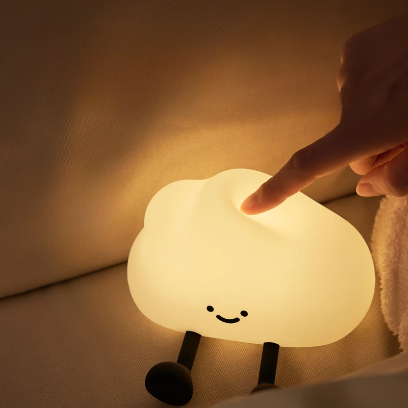 Cloud-shaped night light with a smiling face being touched by a hand in a warm setting.
