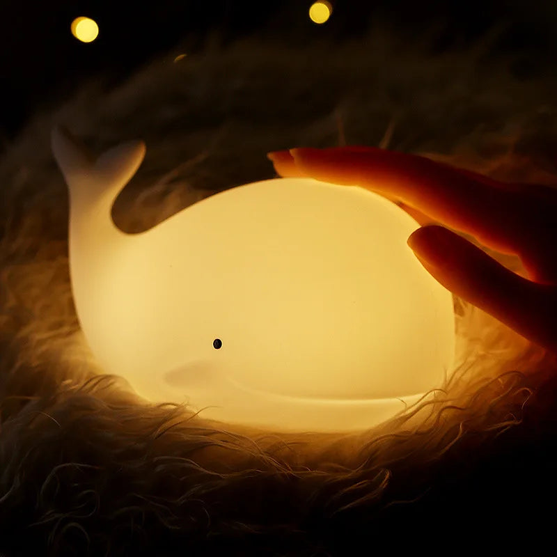 LED Lamp shaped like a whale glowing in a blanket with a human hand turning the lamp on