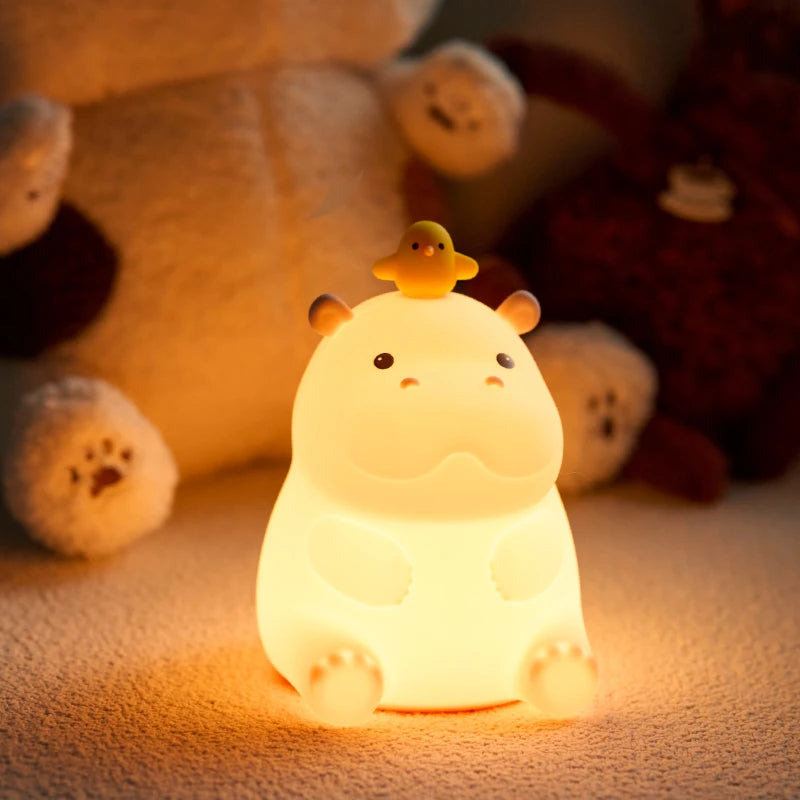 Cute Teacup hippo-shaped night light with a duck on its head, surrounded by plush toys.