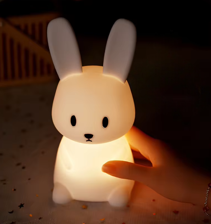 LED Night Light Lamp rabbit sitting on a soft bed and someone holding its body
