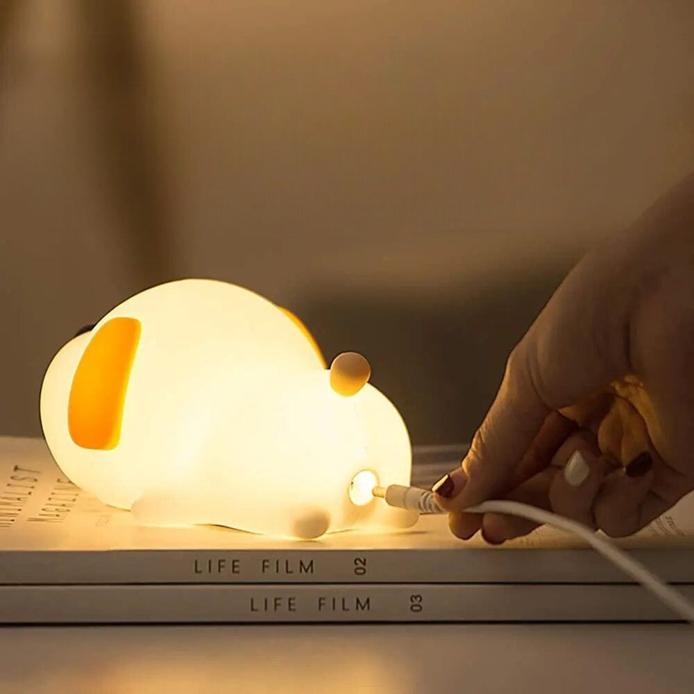 Dog shaped Led Night light lamp laying on two books with someone plugging in the charger