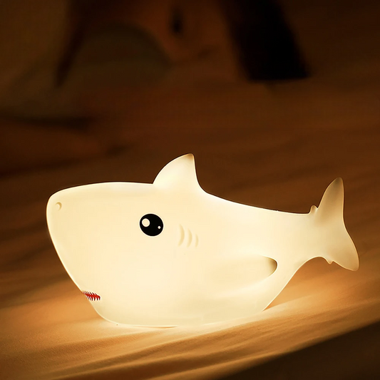 Shark-shaped night light emitting a warm glow on a wooden surface.