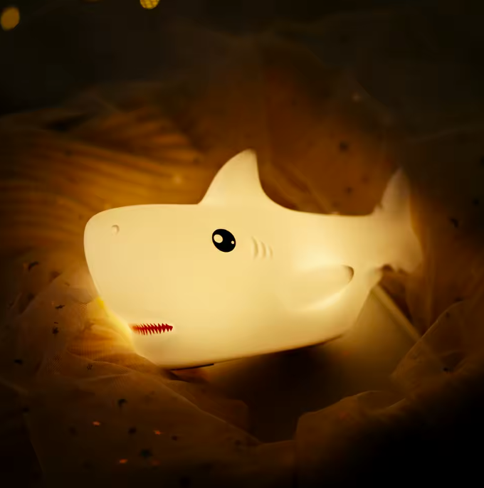 Shark-shaped night light emitting a warm glow on a soft surface.