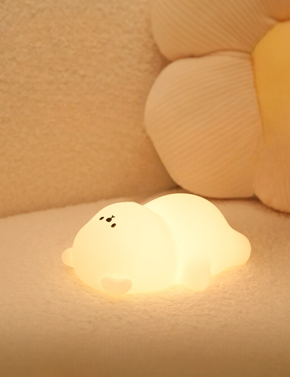 Glowing LED lamp shaped like a chubby bear lying on a soft couch with a sunflower pillow in the background