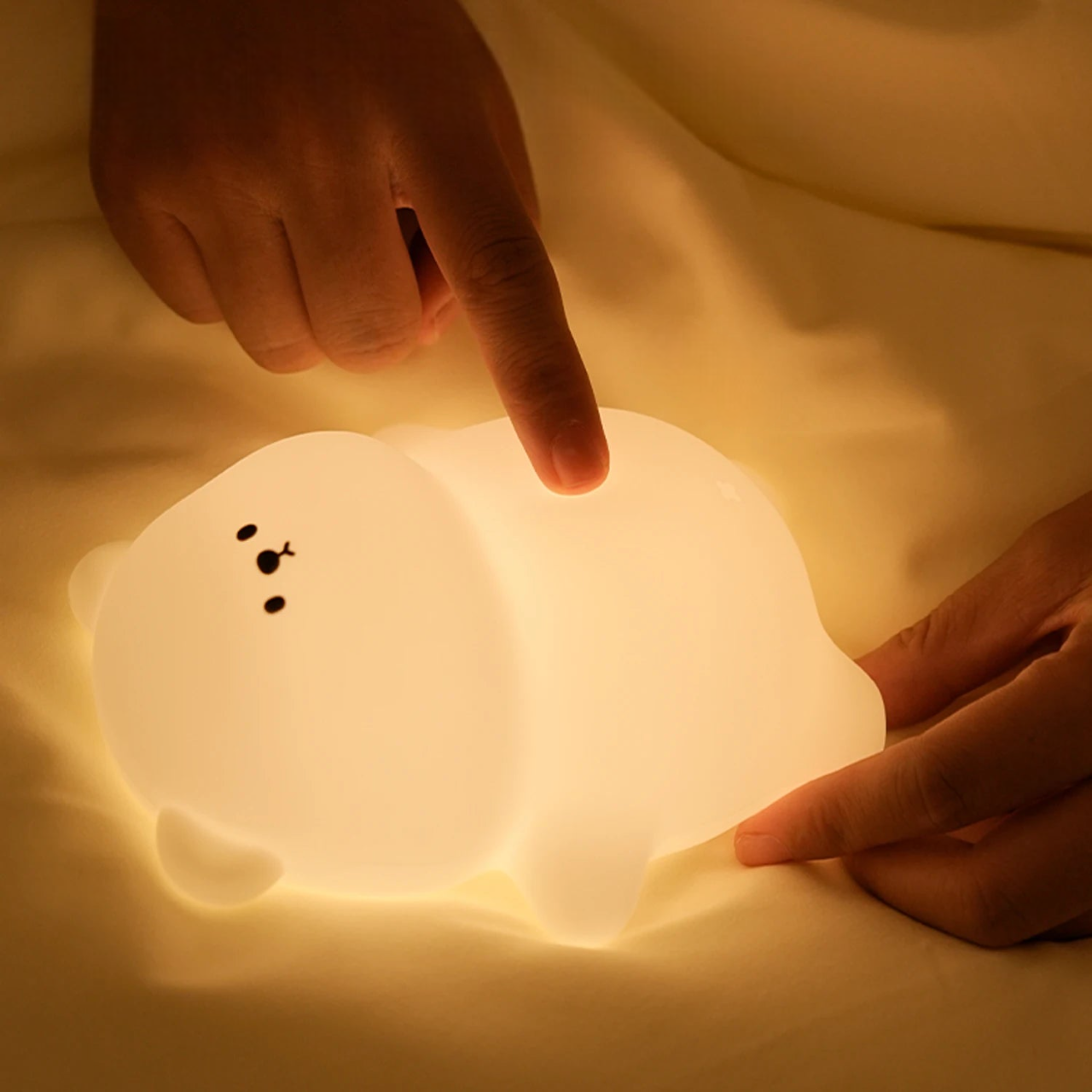 Soft LED lamp glowing on a bed shaped like  bear with a big squishy belly being poked in the belly by a child's hand