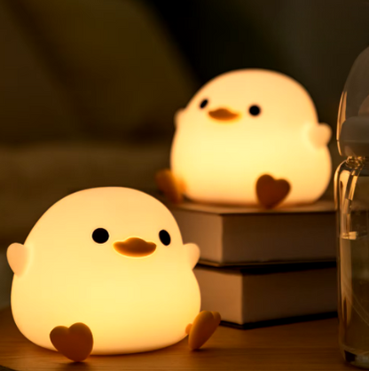 Two LED Night Light Lamp ducks sitting on top of a table with books