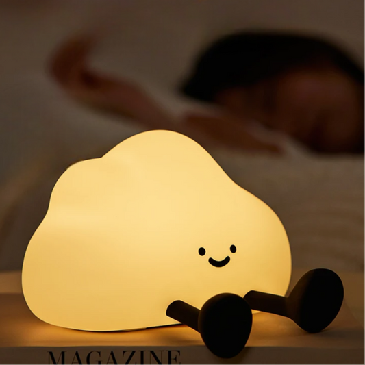 Cloud-shaped night light with a smiley face on a magazine in a dimly lit room.