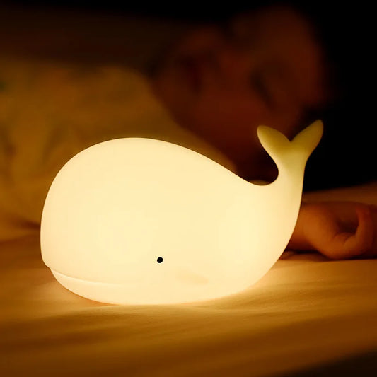 Cozy LED Lamp shaped like a Whale glowing next to sleeping baby on a bed
