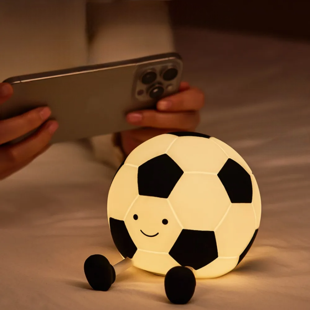 Light-up soccer ball on a bed, person using phone in the background