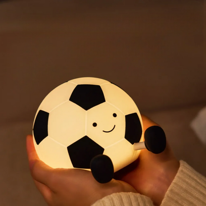 Light-up soccer ball with a smiling face held in a hand against a warm background