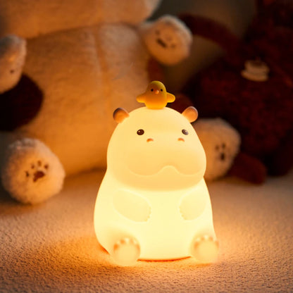 Cute Teacup hippo-shaped night light with a duck on its head, surrounded by plush toys.