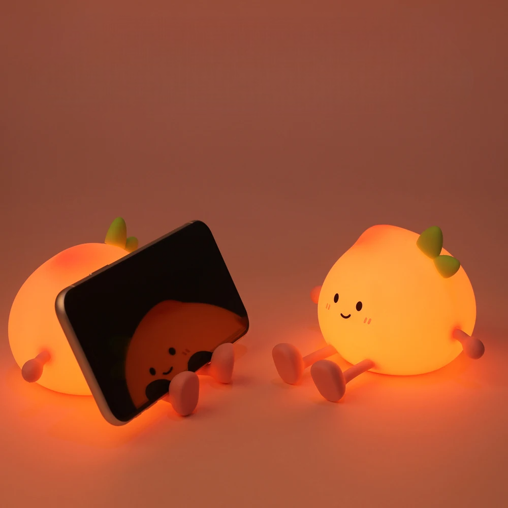 Two cute peach-shaped night lights with a smartphone stand on a warm-toned background.