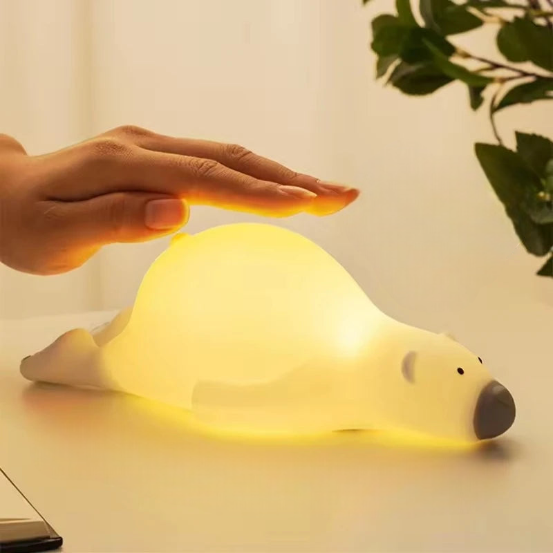 Cubby polar bear shaped LED lamp lying face down on a table with a human hand tapping the light on