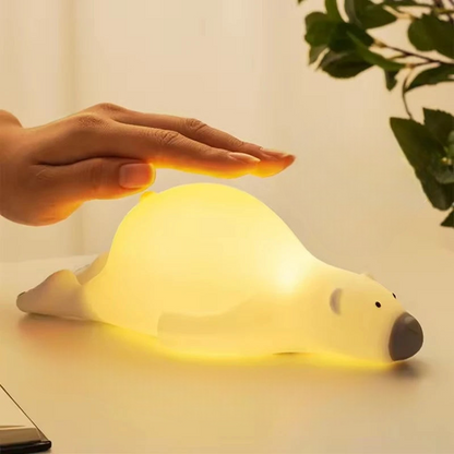 Cubby polar bear shaped LED lamp lying face down on a table with a human hand tapping the light on