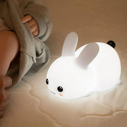 Bunny LED Lamp Glowing warmly next to a baby on a bed