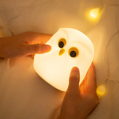 Hand holding a glowing snowy owl-shaped night light on a soft fabric background by cozzy glow 