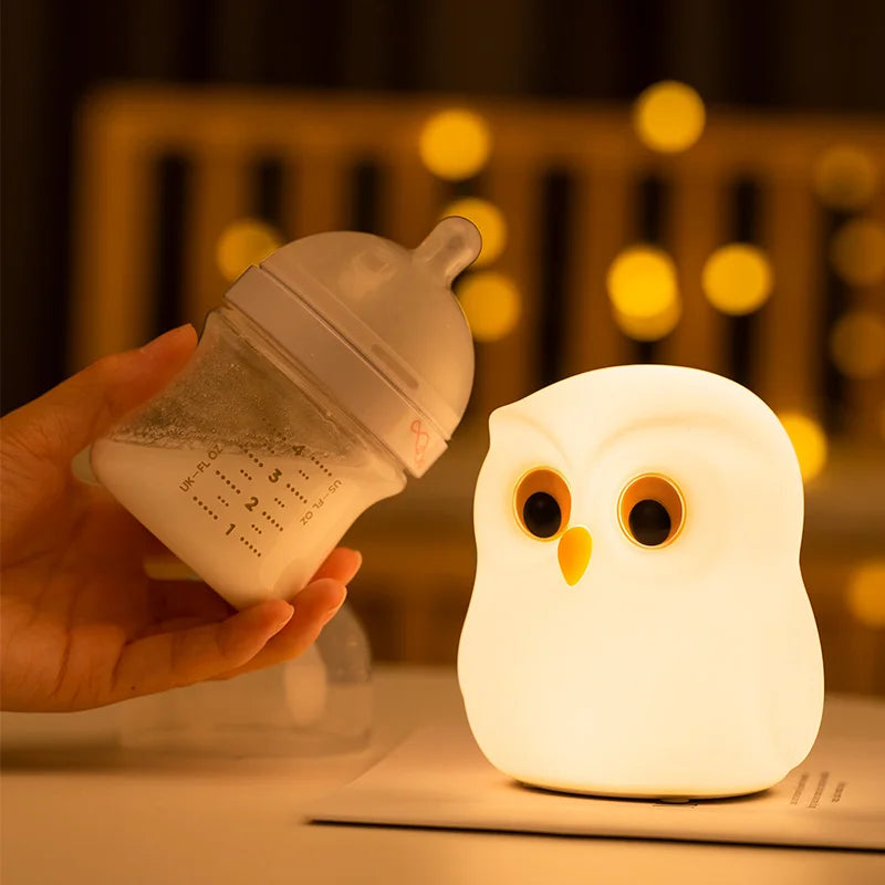 Hand holding a baby bottle next to an snowy owl-shaped night light on a blurred background by cozzy glow